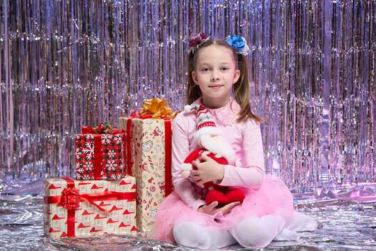 A little girl is sitting in the living room near the Christmas tree with Santa Claus in her hands, New Year's magic