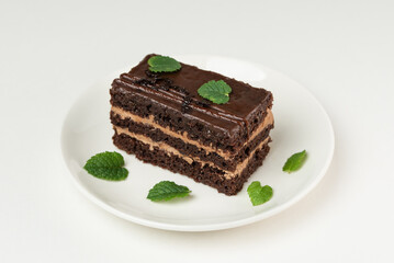 Chocolate biscuit cake with cream and frosting on a white plate isolated on a white background