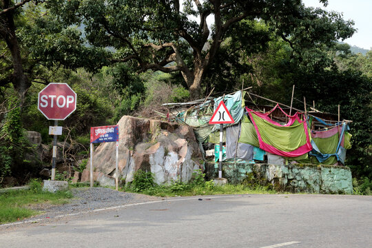 A small, rustic structure draped with colorful fabrics, nestled in a lush, green forest with a hand pump by the entrance.