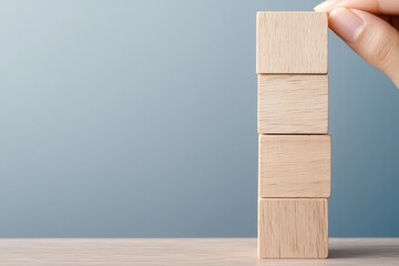 Hand stacking wooden blocks on a table against a light blue background.