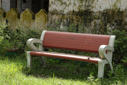 A quiet, charming spot with a red bench amidst lush greenery, set beside an old, vine-covered house. The scene exudes a sense of calm and nature&rsquo;s embrace.