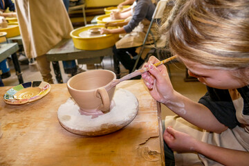girl's hands paint a cup with a brush, ceramic product, master class, workshop, potter