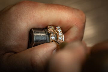 Jeweler puts diamond to golden wedding luxury ring. Selective focus. Macro photo.