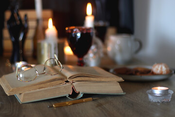 Books, lit candles, red wine, snacks and various deocration on the table. Dark academia or Halloween concept. Selective focus.