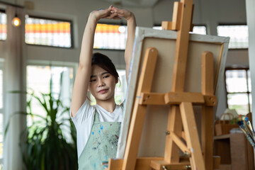 Talented Female Artist Painting on Canvas in Bright Studio with Natural Light and Greenery in the Background © wichayada
