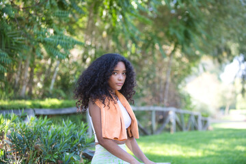 Naklejka premium Young, beautiful, Latin, brunette woman with curly hair, dressed in sports clothes and wearing a towel around her neck to dry her sweat, is sitting on a wooden fence. Concept of sport and health.