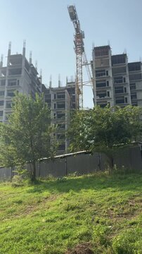 Construction site with a crane. Multiple story building with grey structure and crane. Apartments under construction with a crane.