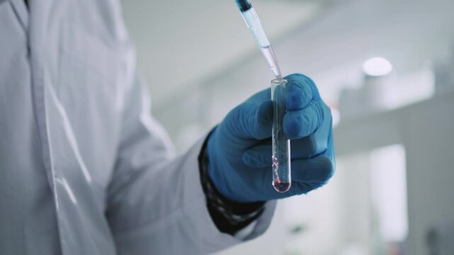 A hands scientist with protective gloves holds a tube and puts liquid inside a light laboratory. Medicine, biotechnology, chemistry
