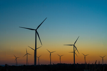 Wind turbines use wind to convert electricity into electricity at wind farms during sunset, a clean energy concept.
