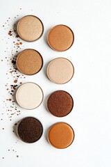 Fototapeta premium Various colored powders in circular containers arranged top view on white surface, scattered powder around