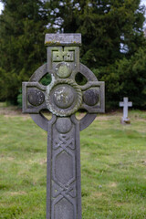 Old weathered Celtic Cross with decorative patterns, moss covered in old churchyard