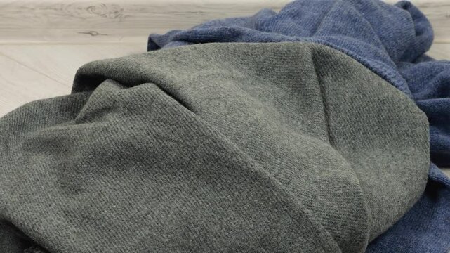 Knitted sweaters, scarves, woolen hats in gray-blue tones are thrown on the floor in the room. The theme of washing, sorting clothes and cleaning the house.