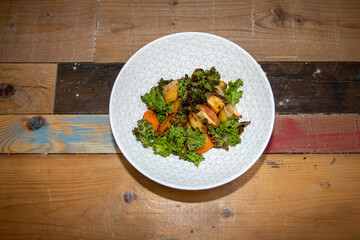 A delicious plate of Roasts Roots with Apple Kale and Crispy Seeds on a wooden kitchen table or work top