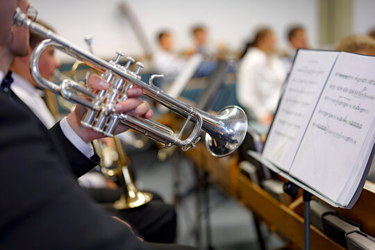 A musician in an orchestra plays a musical composition on a trumpet in an orchestra.