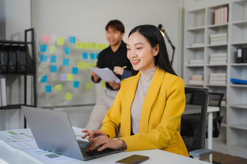 Focused Collaboration: Young businesswoman working on laptop in modern office with colleague in...