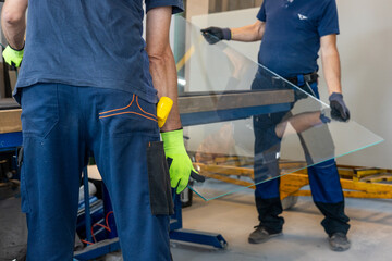 Glaziers place a large pane of glass on a table in the glassworks