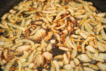 Crispy Fried Onion Bits with oil in the pan. Deep fried onion. Homemade frying onion in a black skillet on the gas oven. Top view. Golden sauteed onions. 4K Close up. Preparing dinner. Cooking at home