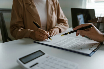 Fototapeta premium Businesswoman is signing a contract while being assisted by a realtor who is pointing at the document
