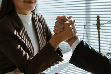 Two business professionals are arm wrestling in their office with a scale of justice in the...