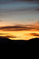 Luna menguante tras las nubes, al alba con de siluetas de montañas