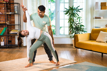 Indian couple practicing yoga, husband assists wife with her one side bend pose happily