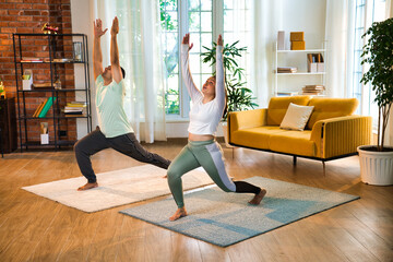 Indian couple happily practicing standing Virabhadrasana pose at home, embodying strength
