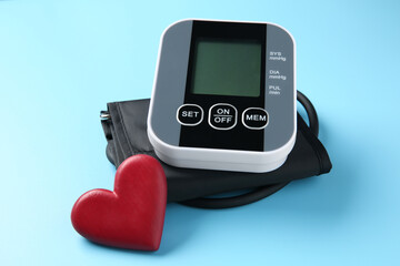 Blood pressure measuring device and heart figure on light blue background, closeup