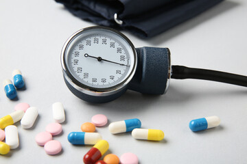 Blood pressure measuring device and pills on light grey background, closeup