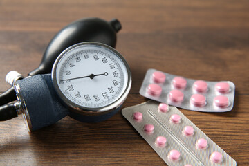 Blood pressure measuring device and pills on wooden table, closeup