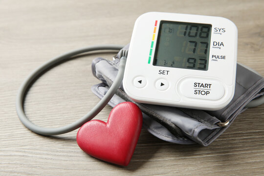 Blood pressure measuring device and heart figure on wooden table, closeup