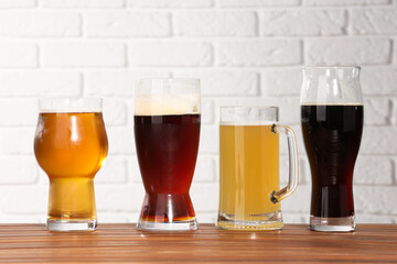 Glasses with different types of beer on wooden table against white brick wall