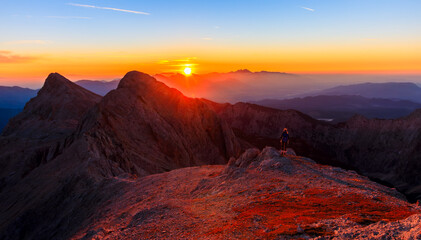 hiking girl stands on a mountain during sunrise against the sun and enjoys the warm morning sun with beautiful mountains golden hour
