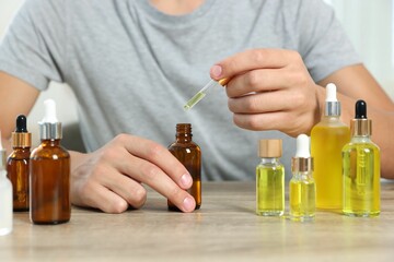 Young man dripping CBD tincture into bottle from dropper at wooden table, closeup