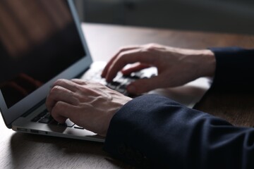 Businessman using laptop at wooden table indoors, closeup. Modern technology