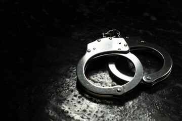 Metal chain handcuffs on black table, closeup. Space for text