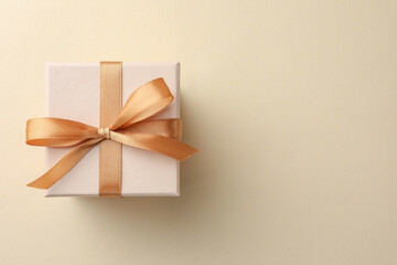 Beautiful gift box with golden bow on beige background, top view. Space for text