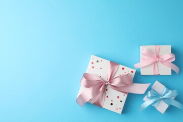 Gift boxes with bows on light blue background, flat lay. Space for text