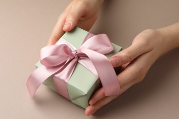 Woman holding gift box with pink bow on beige background, closeup