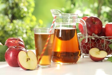 Tasty apple juice in glass, jug and fresh fruits on white table outdoors