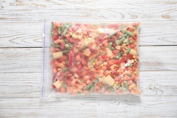 Mix of frozen vegetables in plastic bag on wooden table, top view