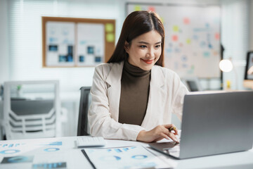 Asian businesswoman is smiling while working on a laptop computer in an office