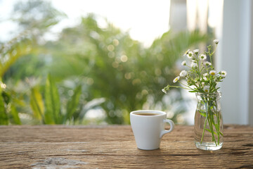 White coffee cup with daisy on wooden table under sunlight on wood table