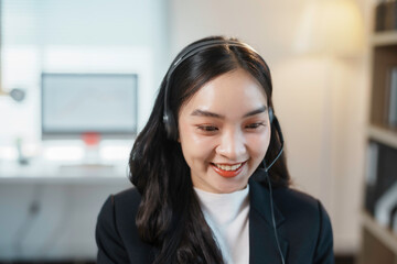 Asian businesswoman is smiling while wearing a headset during an online meeting at work