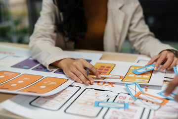 Web designers are using colored paper to plan a mobile app interface, creating a wireframe layout