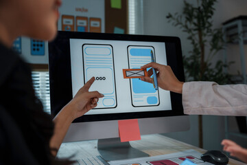 Two web designers are working on a user interface for a mobile application, placing elements on a...