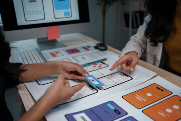 Two uiux designers are discussing over mobile app interface wireframe design prototypes on table at modern office