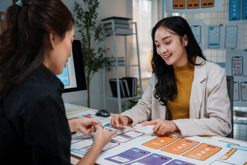 Fototapeta premium Two female uiux designers are discussing over a new mobile application interface wireframe design in the office