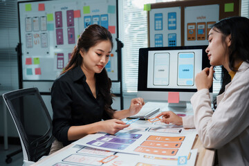 Two asian women working together on a user interface for a mobile application, discussing different...