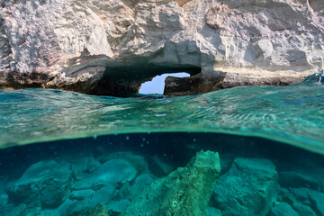 Underwater split photo of small cove and arch rock formations near  famous for colourful boat houses area of Karas, Kimolos island, Cyclades, Greece