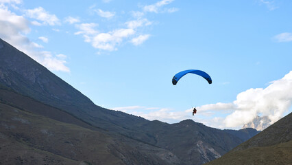 Panoramic view of the mountainous landscape with a paraglider in the air against a cloudy sky.